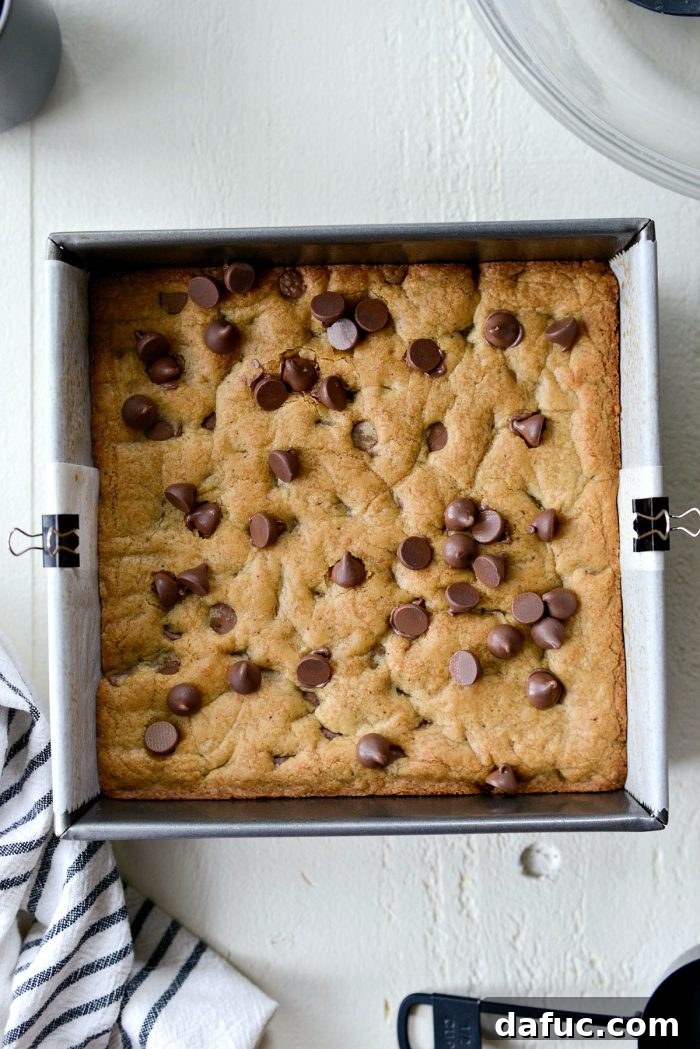 Golden Brown Butter Chocolate Chip Blondies 18 Freshly baked brown butter chocolate chip blondies cooling in the pan, with extra chocolate chips sprinkled on top.