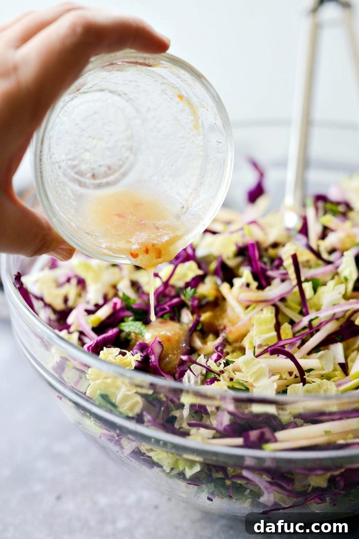 Vibrant Grilled Thai Chicken Salad 16 Reserved healthy Thai dressing being poured over the salad ingredients and sliced chicken in a large mixing bowl.