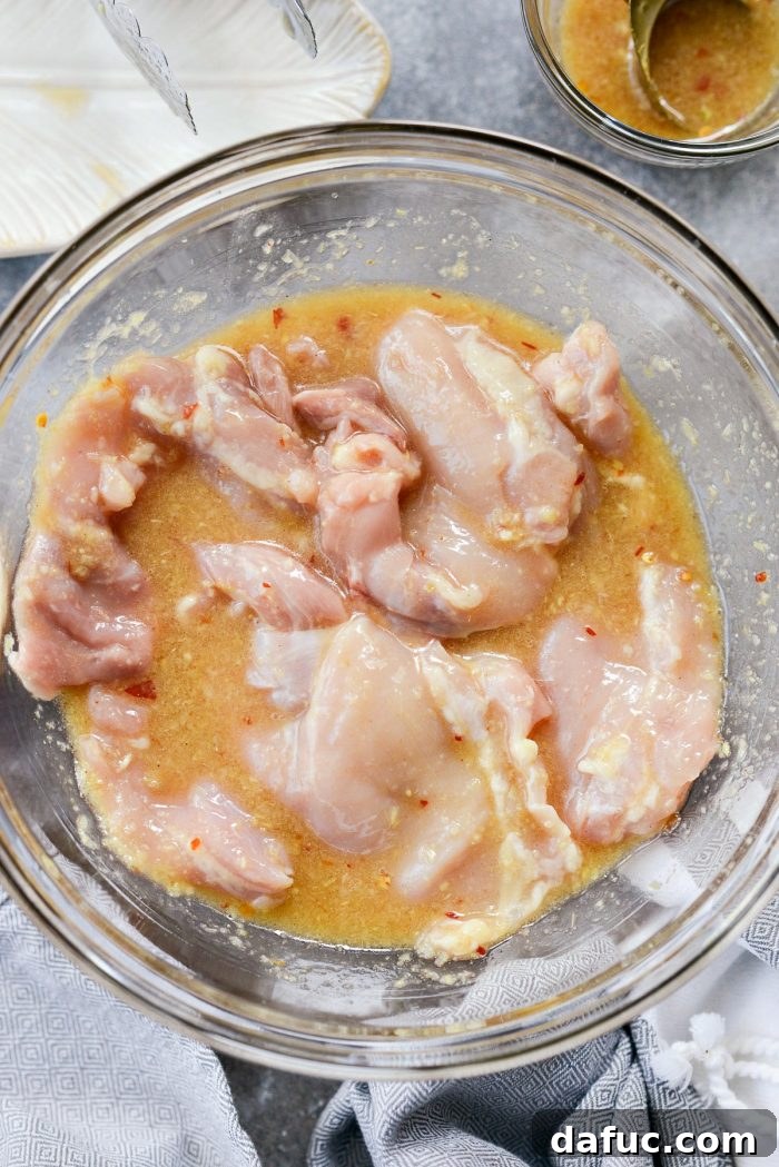 Vibrant Grilled Thai Chicken Salad 10 Boneless, skinless chicken thighs added to the Thai marinade in a mixing bowl, being tossed to coat evenly.