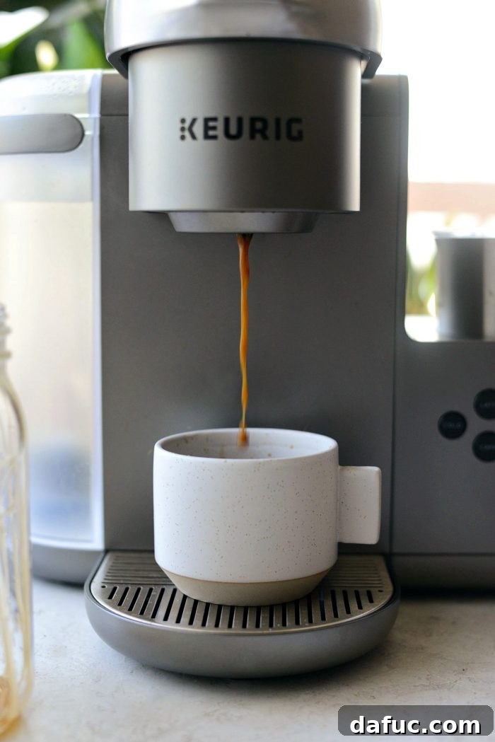 Velvet Caramel Vanilla Chill 10 A Keurig coffee maker actively brewing a shot of espresso into a cup with vanilla syrup.