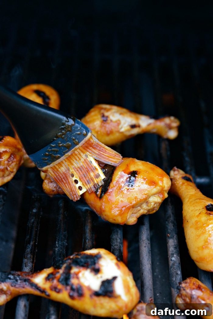 Sticky Sweet BBQ Drumsticks 12 A chicken drumstick being turned on the grill with tongs, while another is being brushed with barbecue sauce, illustrating the basting process.