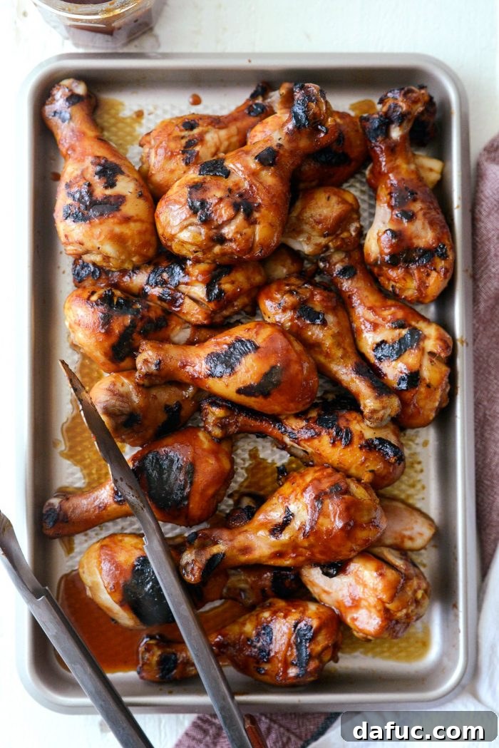 Sticky Sweet BBQ Drumsticks 13 Cooked and saucy chicken drumsticks being removed from the grill and placed back onto a pan for serving.