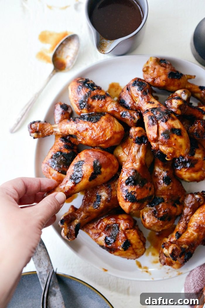 Sticky Sweet BBQ Drumsticks 15 A hand reaching for a piece of easy BBQ chicken drumstick from a large platter, highlighting the appealing readiness of the meal.