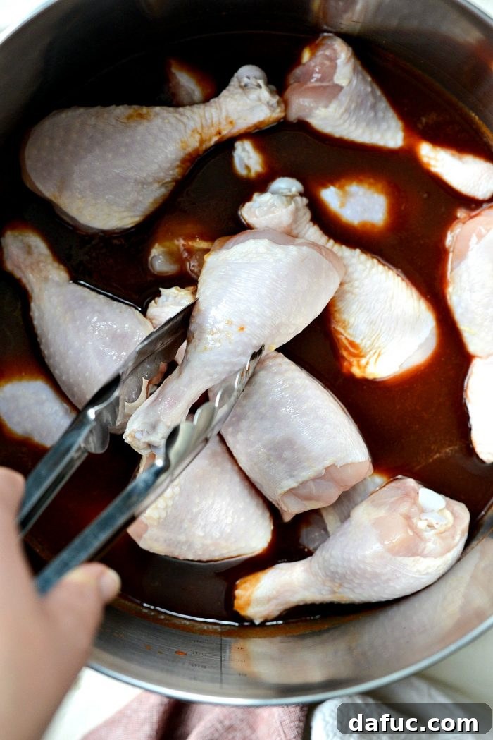 Sticky Sweet BBQ Drumsticks 6 Chicken drumsticks being carefully placed into the simmering homemade barbecue sauce in a large pot using tongs.
