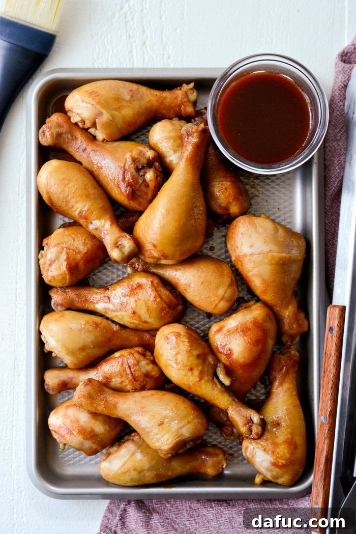 Sticky Sweet BBQ Drumsticks 10 Cooked chicken drumsticks being transferred from the pot of sauce to a rimmed baking sheet, with a cup of reserved sauce alongside.