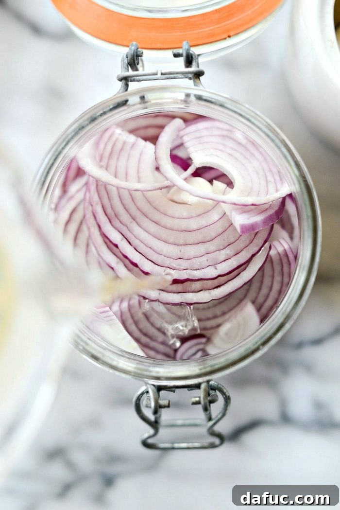 Zesty Quick Pickled Red Onions 7 Pouring the pickling liquid over thinly sliced red onions in a glass jar