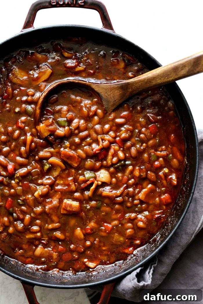 One Pot Wonder Baked Beans 2 wooden spoon in red pot with one pot wicked baked beans, showcasing the rich texture and vibrant colors of the dish