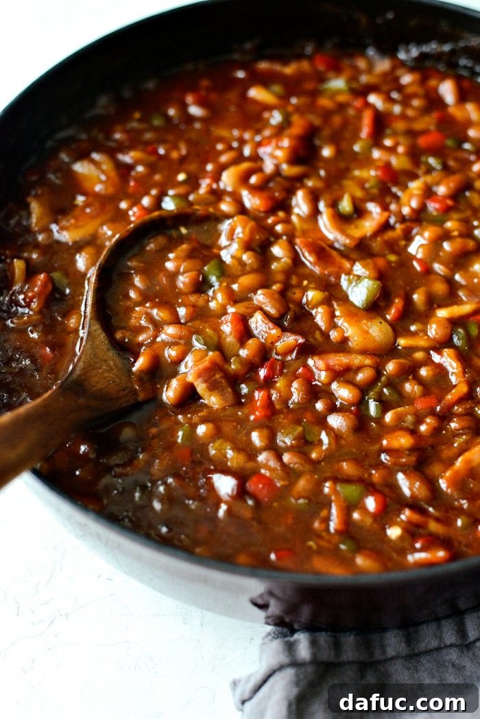 One Pot Wonder Baked Beans 3 side shot of a wooden spoonful of one pot wicked baked beans, highlighting the chunky ingredients