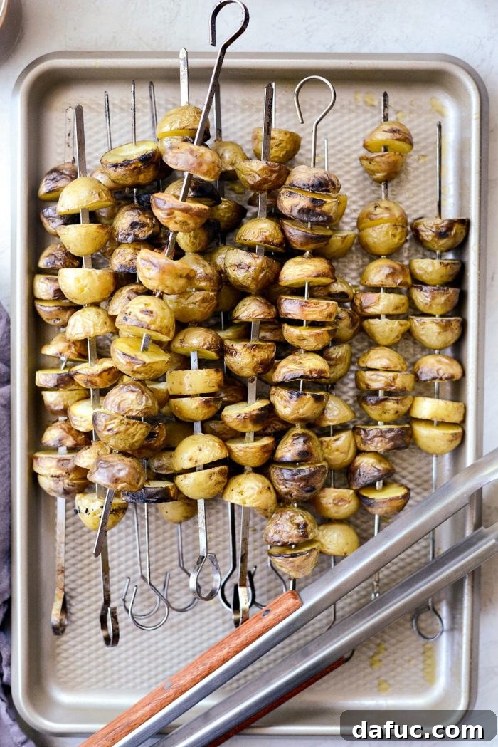 Grilled potatoes on skewers cooling on a baking sheet.