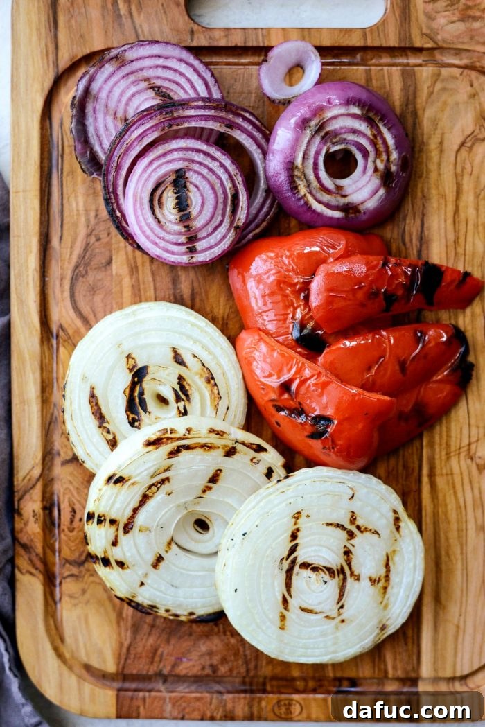 Grilled bell peppers and onions cooling on a cutting board.