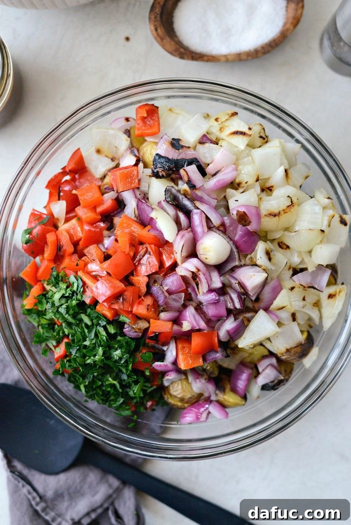 Grilled potatoes, chopped peppers, onions, and minced parsley in a large glass mixing bowl.