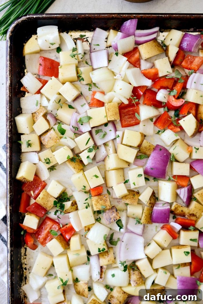 Smoked Brisket Breakfast Hash 5 Fresh thyme leaves and chopped oregano being sprinkled over diced vegetables on a baking sheet before roasting.