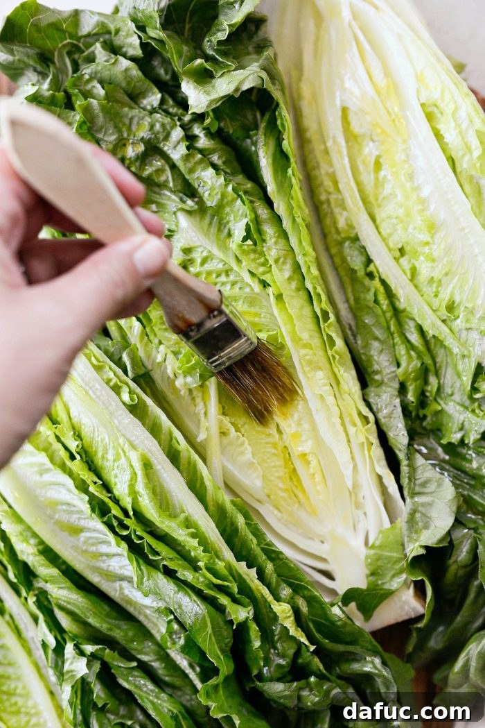 Cut side of romaine lettuce halves being brushed with roasted garlic olive oil
