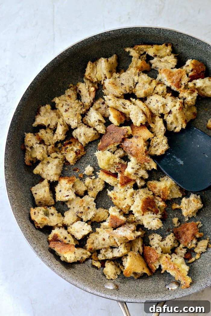 Hand-torn pieces of whole grain bread toasting in a skillet with bacon grease
