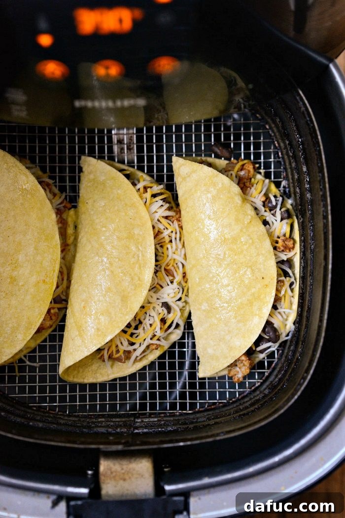 Three folded chipotle chicken black bean tacos placed in the basket of an air fryer, ready to cook.