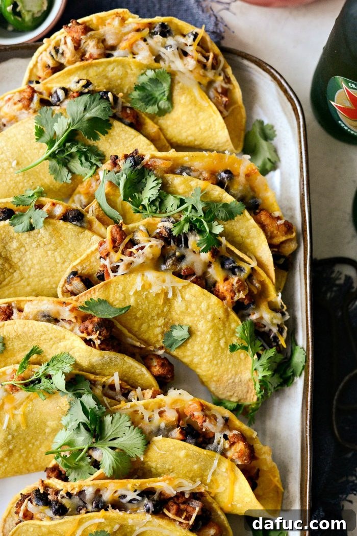 A close-up of a serving of crispy air fried chipotle chicken black bean tacos, garnished with fresh cilantro and lime.