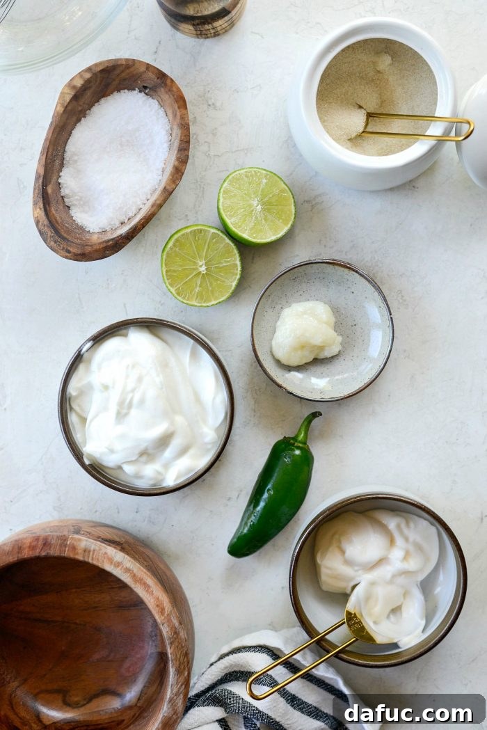 Ingredients for jalapeño crema including Greek yogurt, mayonnaise, a jalapeño pepper, garlic cloves, and a lime.