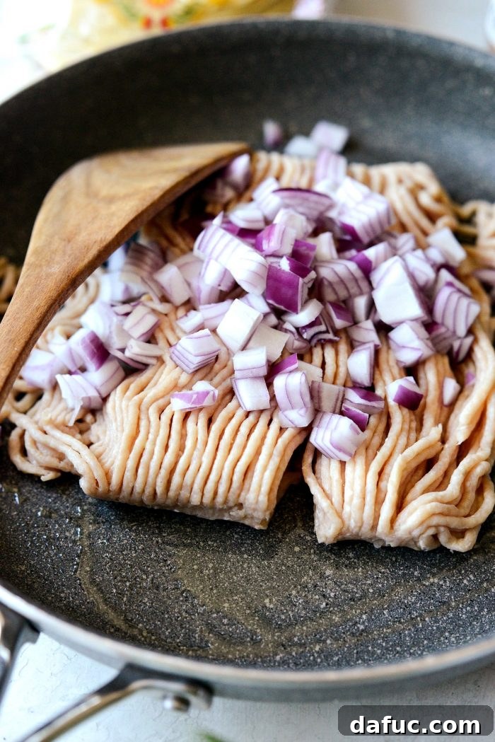 Ground chicken and diced red onion cooking in a nonstick skillet on a stovetop.