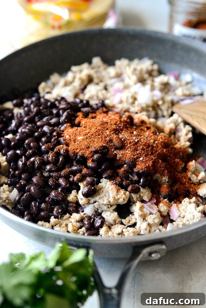 Black beans and smoky chipotle seasoning blend added to the cooked ground chicken and red onion in a skillet.