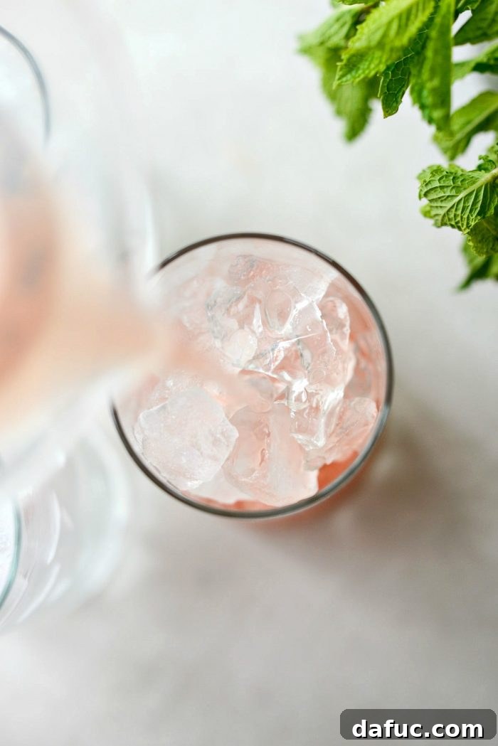 Pouring the refreshing watermelon lemonade from a pitcher into a glass filled with ice.