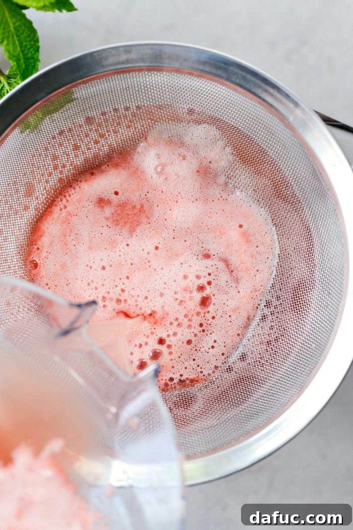 Straining the pureed watermelon lemonade through a fine mesh sieve into a large bowl with a spout, separating pulp from liquid.