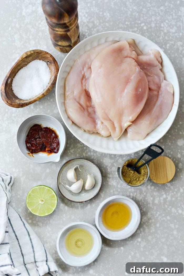 Signature Chipotle Chicken Marinade 3 All the fresh and vibrant ingredients laid out for the chipotle chicken marinade, including whole chipotle peppers in adobo, garlic cloves, fresh limes, a bottle of avocado oil, a jar of honey, and small bowls of ground cumin, kosher salt, and black pepper.