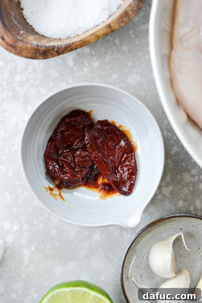 Signature Chipotle Chicken Marinade 4 A small, ceramic bowl filled with dark red, glistening chipotle peppers in adobo sauce, highlighting their rich color, texture, and the saucy coating, ready to be processed for the marinade.