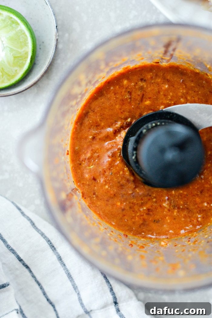 Signature Chipotle Chicken Marinade 7 The blended chipotle chicken marinade in a mini food processor, showcasing its rich, reddish-brown color and a slightly thick, mildly chunky texture, indicating it's perfectly prepared to coat the chicken.
