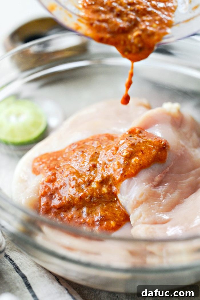 Signature Chipotle Chicken Marinade 8 A vibrant, reddish-brown chipotle marinade being poured generously over uniformly pounded chicken breasts nestled in a clear glass bowl, ensuring each piece is fully covered and ready for flavor absorption.