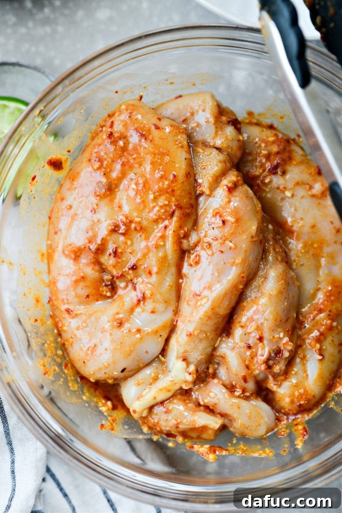 Signature Chipotle Chicken Marinade 9 A close-up view of raw chicken breasts thoroughly tossed and coated in the rich, red chipotle marinade inside a mixing bowl, glistening with flavor and ready to be covered for marination.