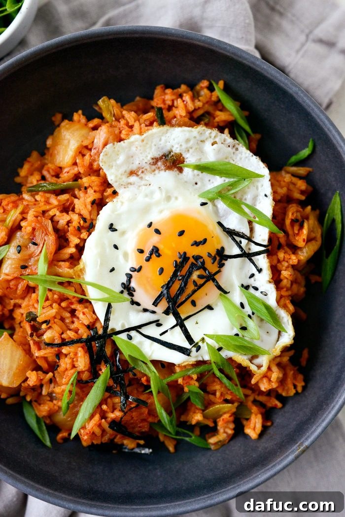 Ultimate Kimchi Fried Rice 17 Kimchi fried rice in a black bowl, beautifully garnished with a fried egg, black sesame seeds, green onions, and nori.