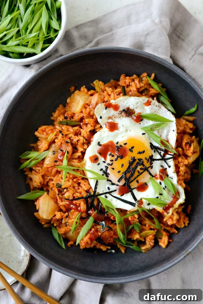 Ultimate Kimchi Fried Rice 18 Kimchi fried rice in a black bowl with a fried egg, a side of gochujang hot sauce, and chopsticks.