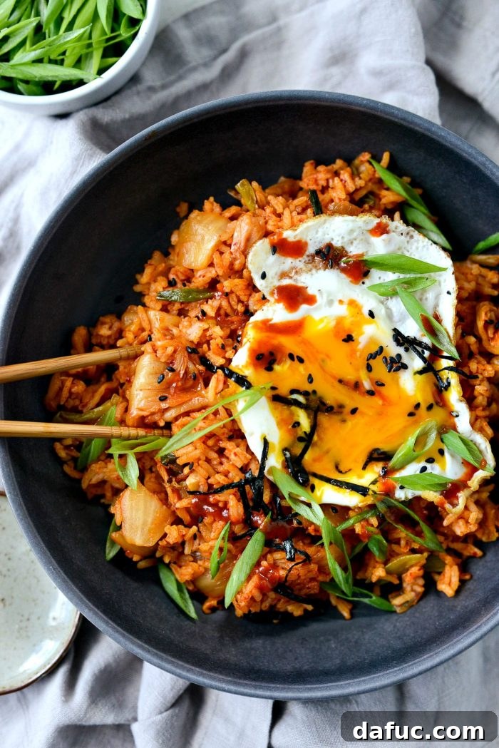 Ultimate Kimchi Fried Rice 19 Chopsticks poised to pick up a delicious bite of kimchi fried rice with a perfect fried egg, showcasing the textures.
