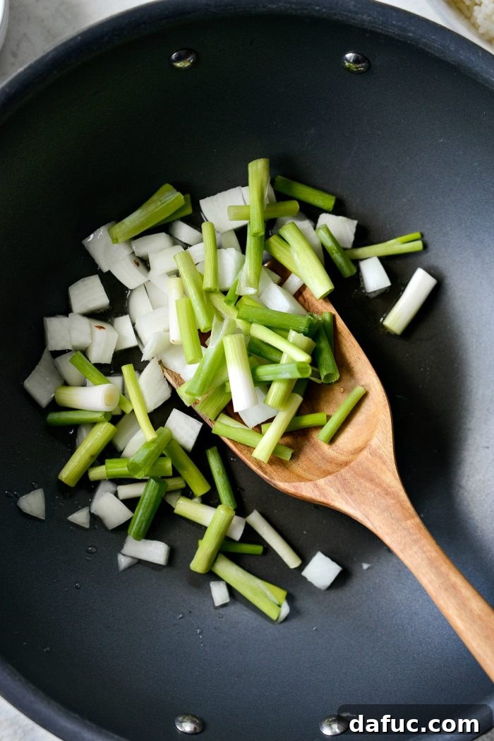 Ultimate Kimchi Fried Rice 7 Adding diced yellow onions and green onion whites to a hot wok with oil.