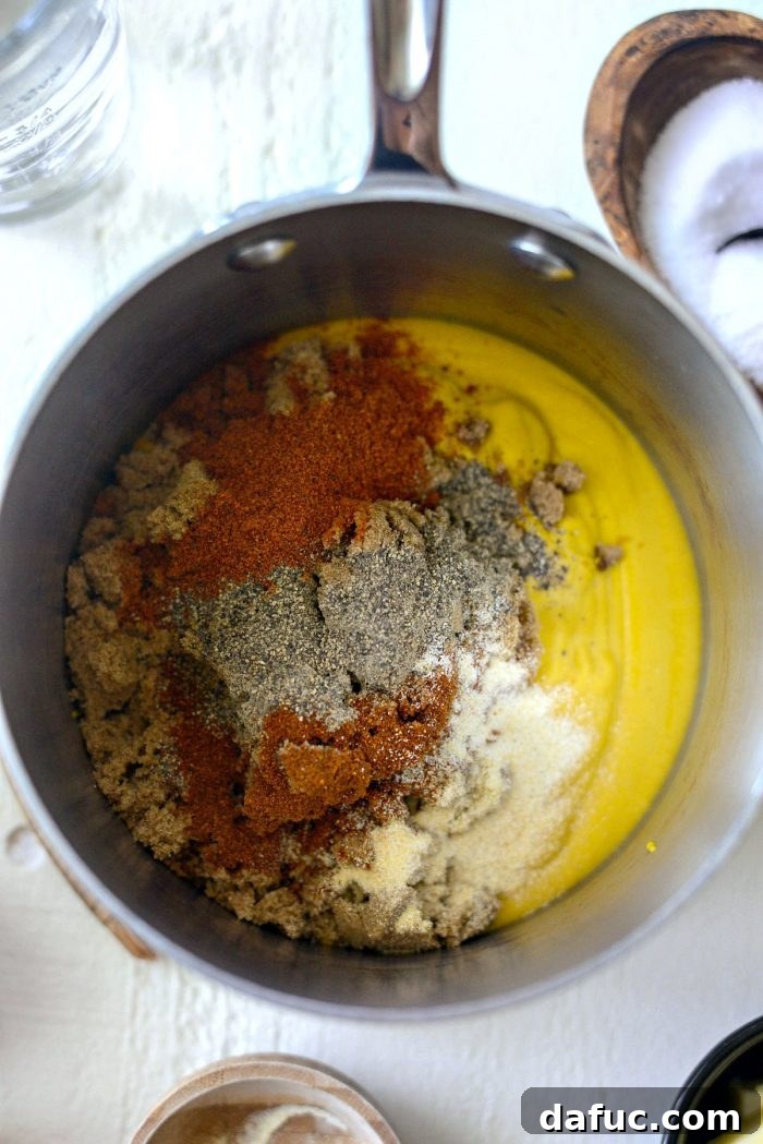Yellow mustard, dark brown sugar, chili powder, black pepper, cayenne, garlic powder, onion powder, and kosher salt in a saucepan, ready for mixing.