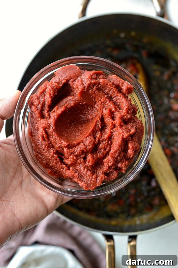 Tomato paste being whisked into the simmering Coca-Cola Habanero BBQ Sauce mixture.
