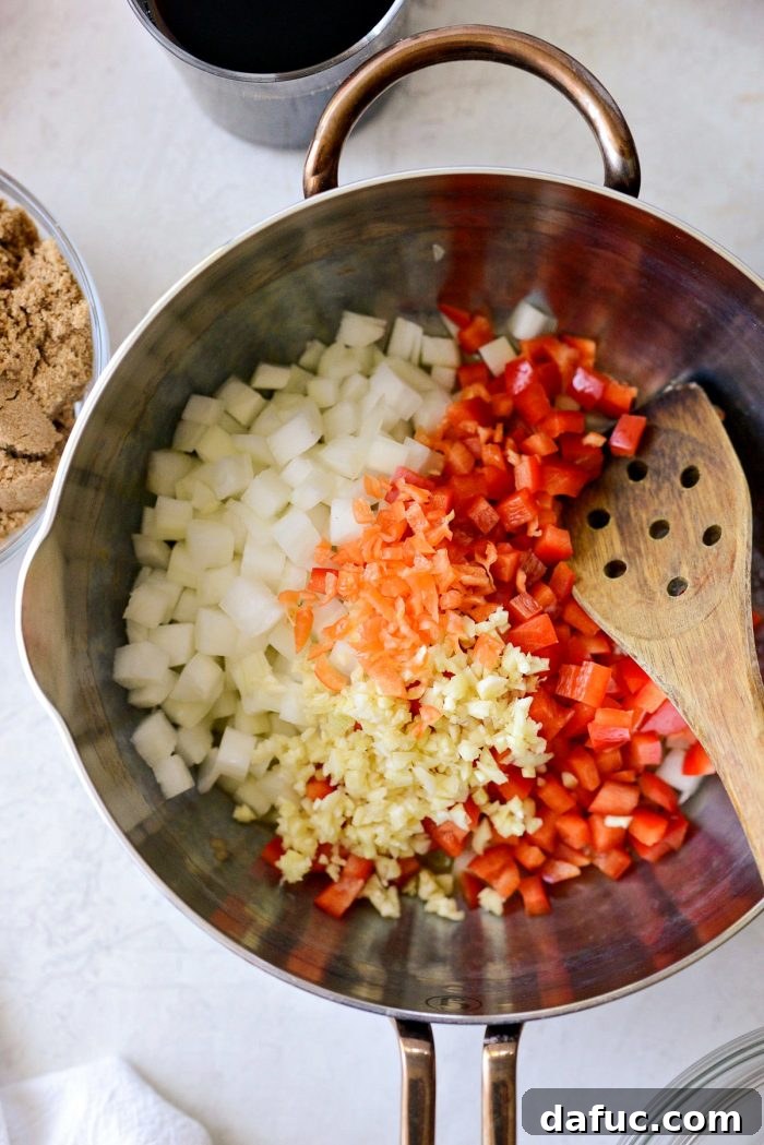 Diced red bell pepper, yellow onion, minced garlic, and habanero pepper simmering in butter in a pan.