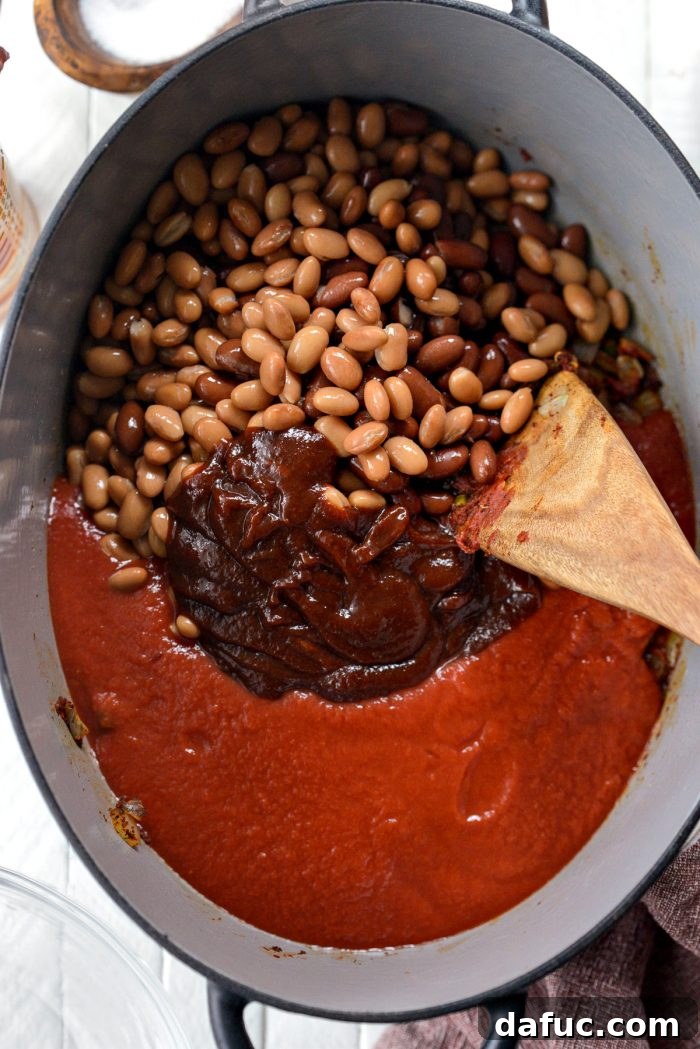 Fireside Smoky Pulled Pork Chili 9 Beans, BBQ sauce, and tomato sauce being stirred into the pot with vegetables and spices
