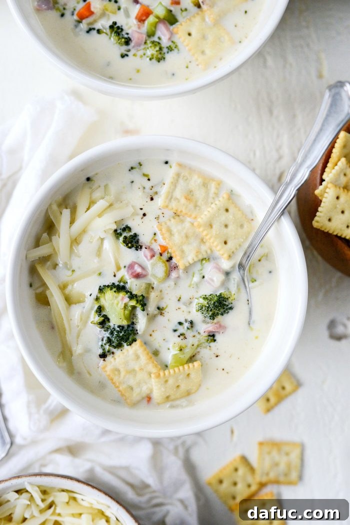 Hearty Ham, Swiss & Broccoli Delight 2 Creamy Broccoli Ham and Swiss Soup in elegant white bowls, ready to be enjoyed with a spoon.