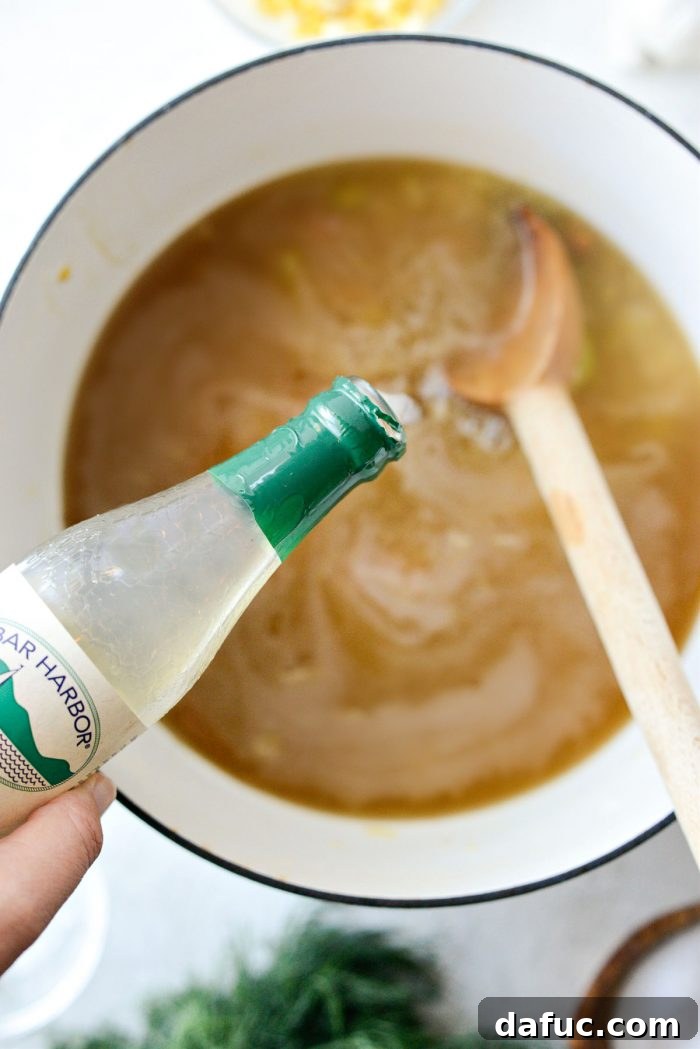 Coastal Catch Salmon Chowder 12 A bottle of clam juice being poured into the soup pot, alongside chicken stock and vegetables.