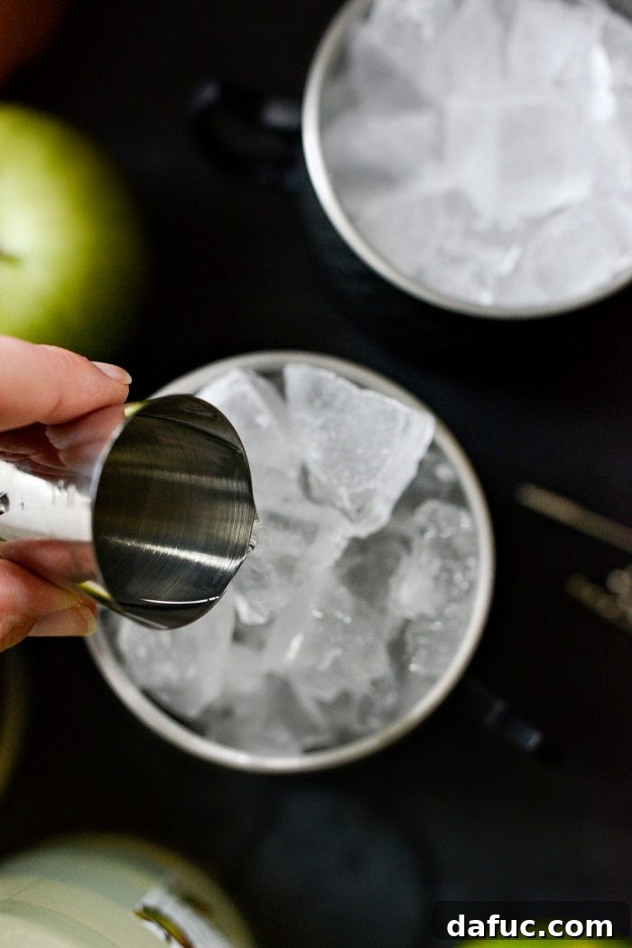 Orchard Mule 6 Pouring apple vodka into an ice-filled copper mug as the first liquid ingredient.