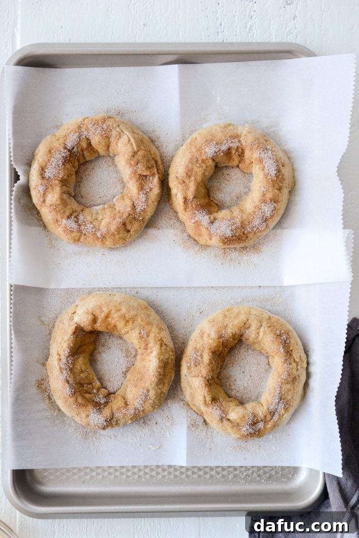 Delicious Air Fryer Pumpkin Spice Bagels 19 Top-down view of four unbaked pumpkin spice bagels, brushed with egg wash and sprinkled with sugar topping, ready for the air fryer.