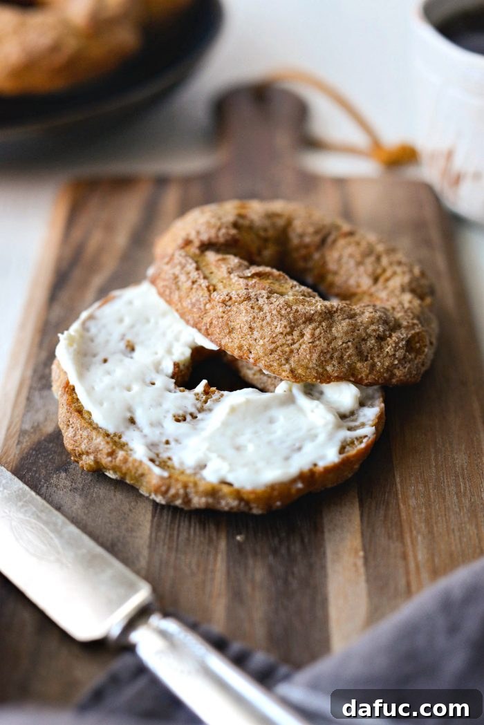 Delicious Air Fryer Pumpkin Spice Bagels 25 Two air-fried pumpkin spice bagels, one whole and one sliced in half, presented on a wooden board.