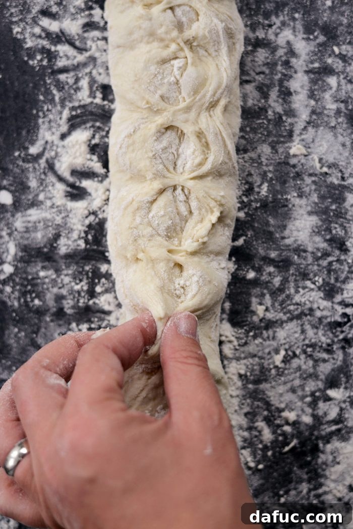 Pinching the dough seam to create tension for a baguette.