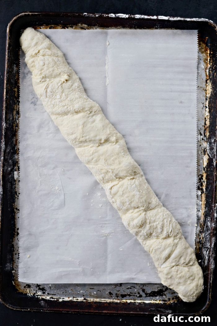 Scoring the top of a baguette with a knife before baking.