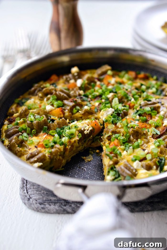 Skillet of Roasted Pumpkin Kale and Feta Frittata with piece missing.