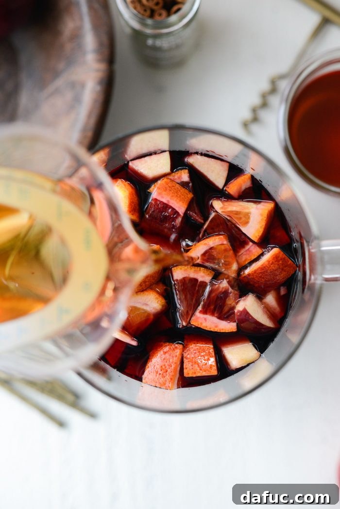 Ruby Fizz Sangria 11 Pouring vanilla brandy into the sangria mixture