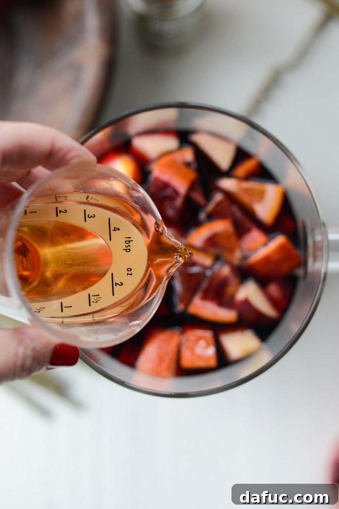 Adding the chilled cinnamon simple syrup to the sangria pitcher