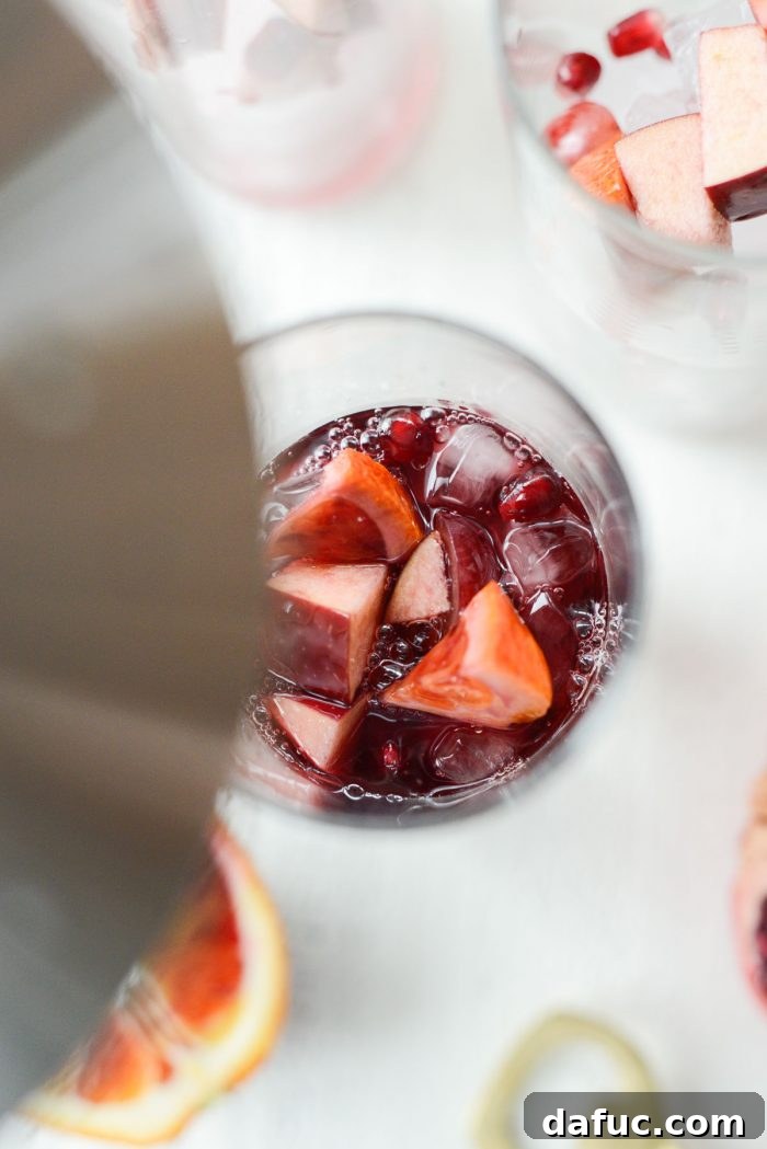 Pouring sangria from a pitcher into a glass filled with ice and fruit