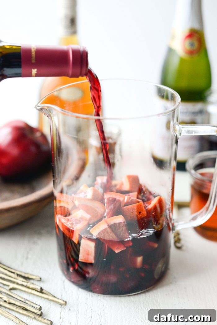 Pouring red wine into a glass pitcher filled with fresh fruit for sangria